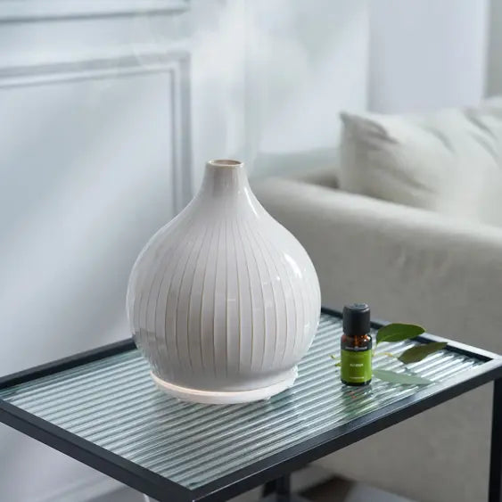 Dyfuzor zapachowy Pistil White 250 ml łączy funkcjonalność dyfuzora ultradźwiękowego z formą dekoracyjnej ceramiki. Jego pełna, harmonijna sylwetka inspirowana kształtem pąka oraz regularne pionowe żłobienia nadają mu rzeźbiarski charakter. Ciepła biel i subtelny pierścień światła przy podstawie wprowadzają do wnętrza spokój, miękkość i elegancję.